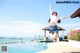 A woman jumping in the air in front of a swimming pool.