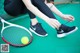 A woman tying up her tennis shoes next to a tennis racket.