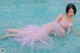 A woman in a pink dress laying on the edge of a pool.