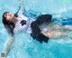 A woman in a white shirt and black skirt floating in a pool.