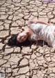 A woman laying on the ground in a dry, cracked field.